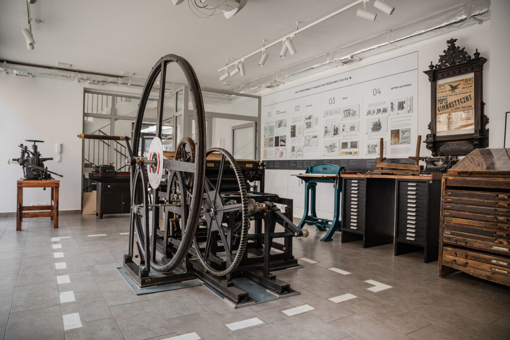 Wnętrze muzeum z zabytkowymi maszynami drukarskimi, szafami na czcionki i ekspozycją poświęconą historii druku i książki.