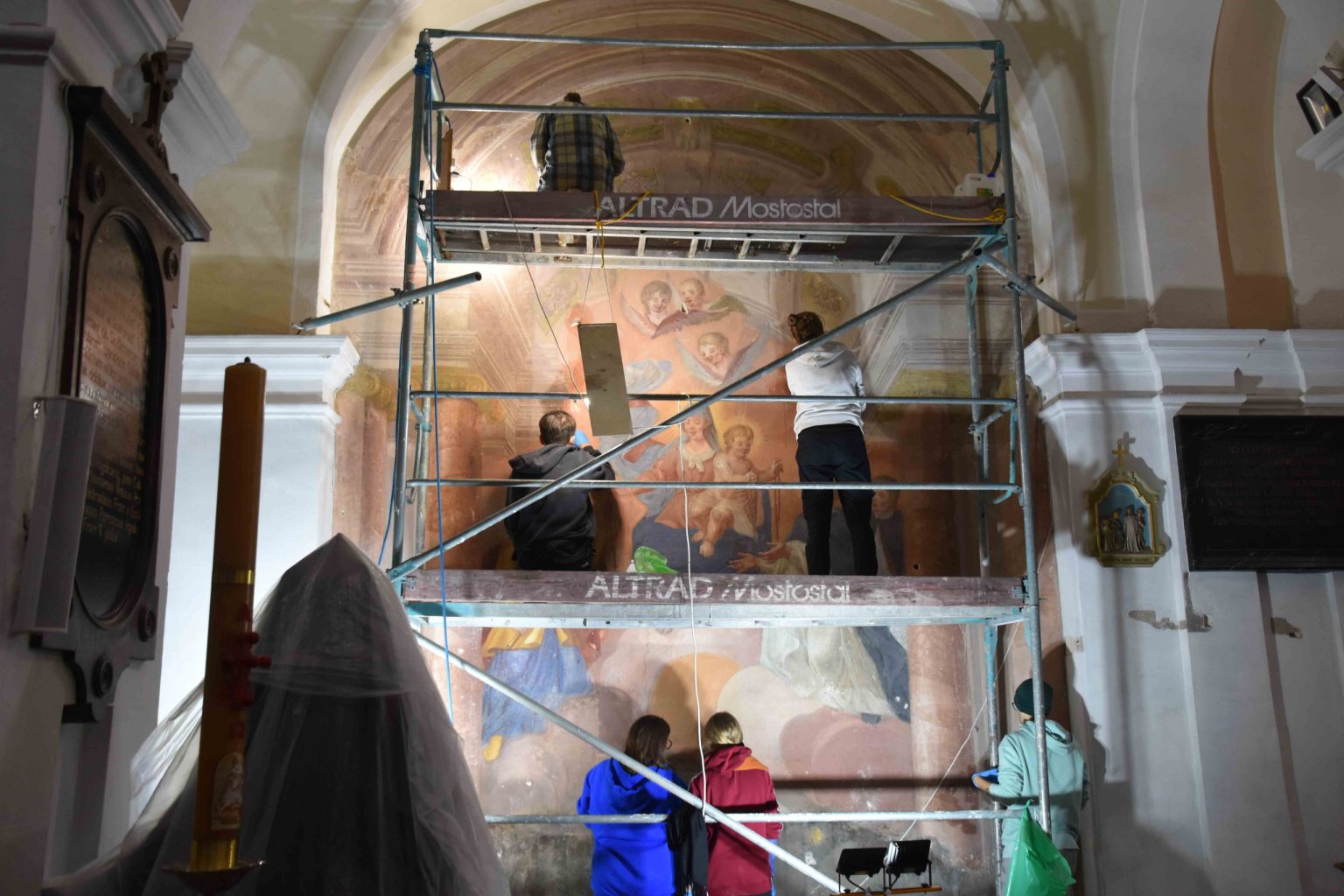 Konserwatorzy pracują przy renowacji malowidła ściennego stojąc na rusztowaniu