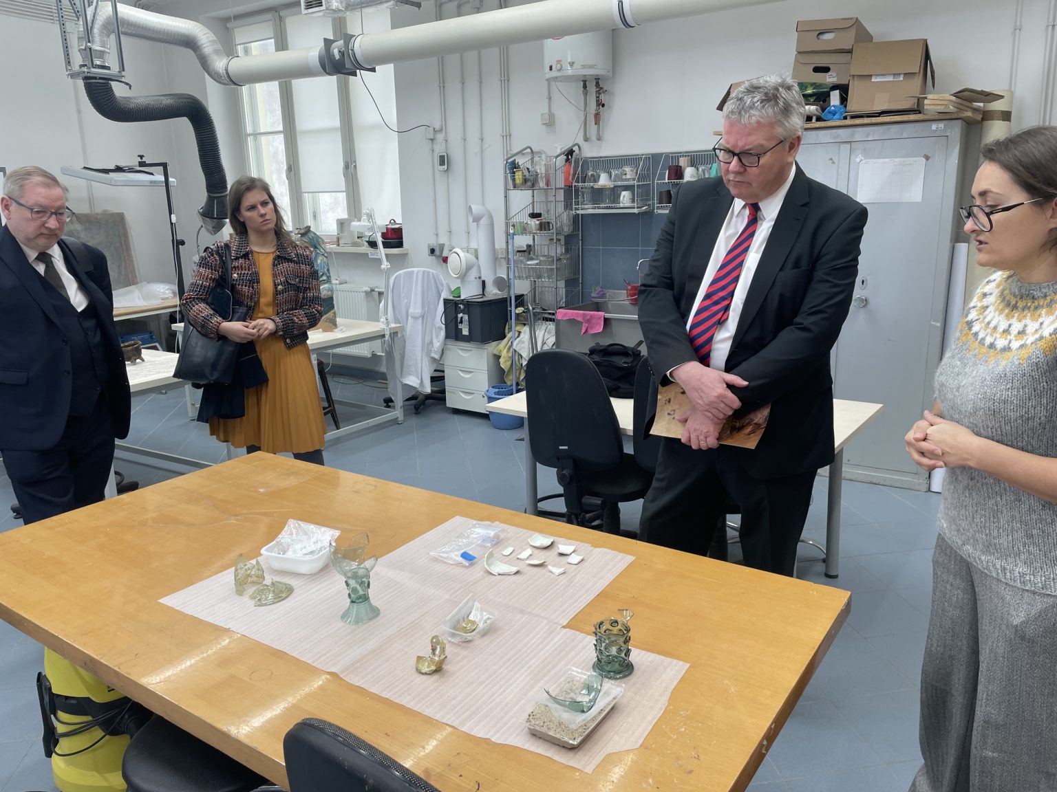 dwóch mężczyzn w czarnych garniturach ogląda obiekty archeologiczne położone na stole