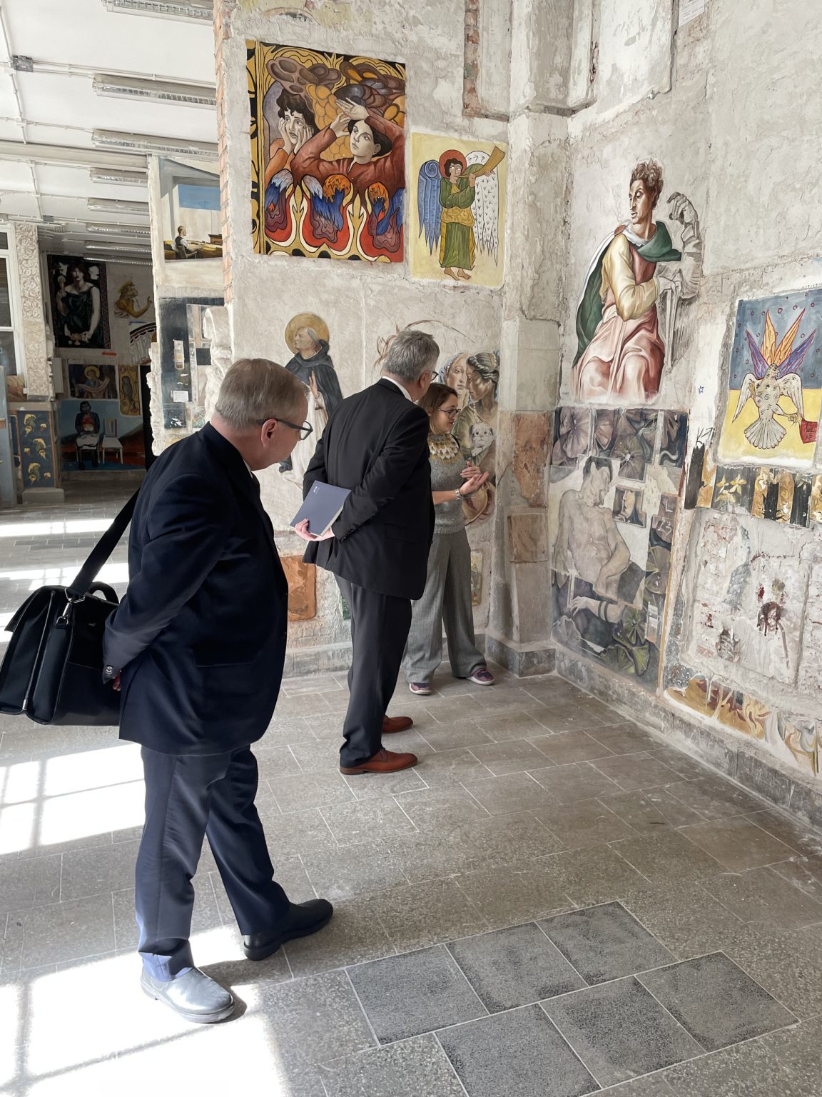 dwóch mężczyzn w garniturach podziwia malowidła ścienne w pracowni