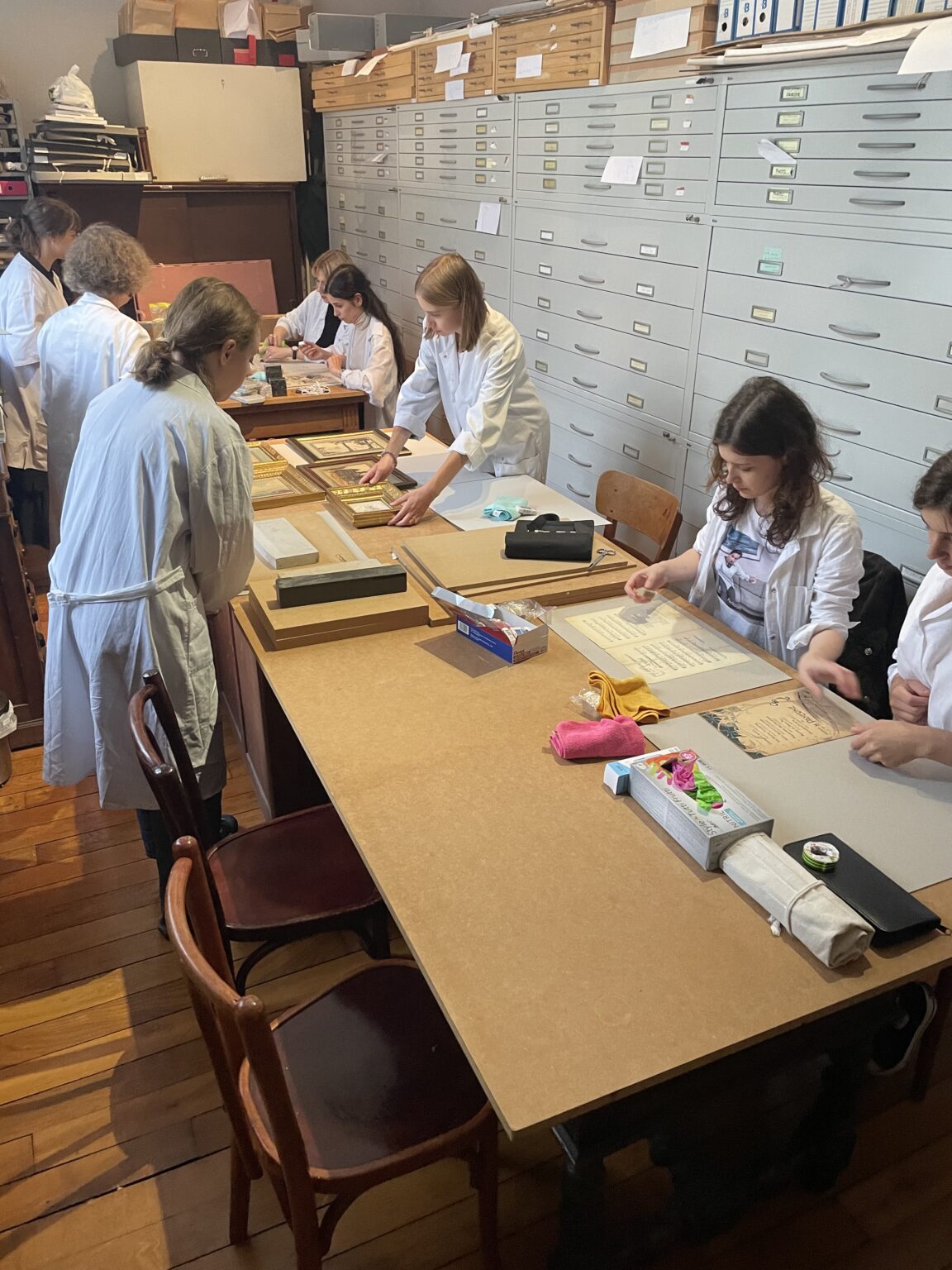 studentki ubrane w białe fartuchy pracują przy zabytkach papierowych.