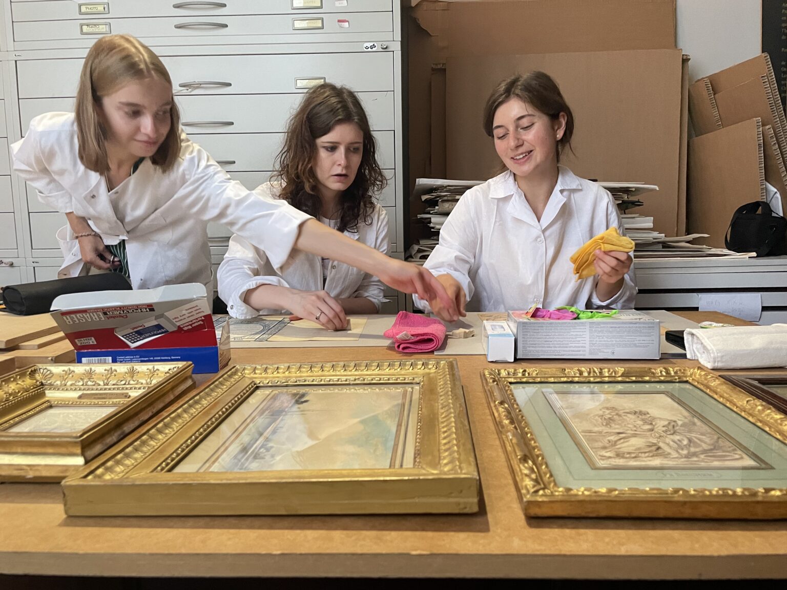studentki ubrane w białe fartuchy pracują przy zabytkach papierowych.