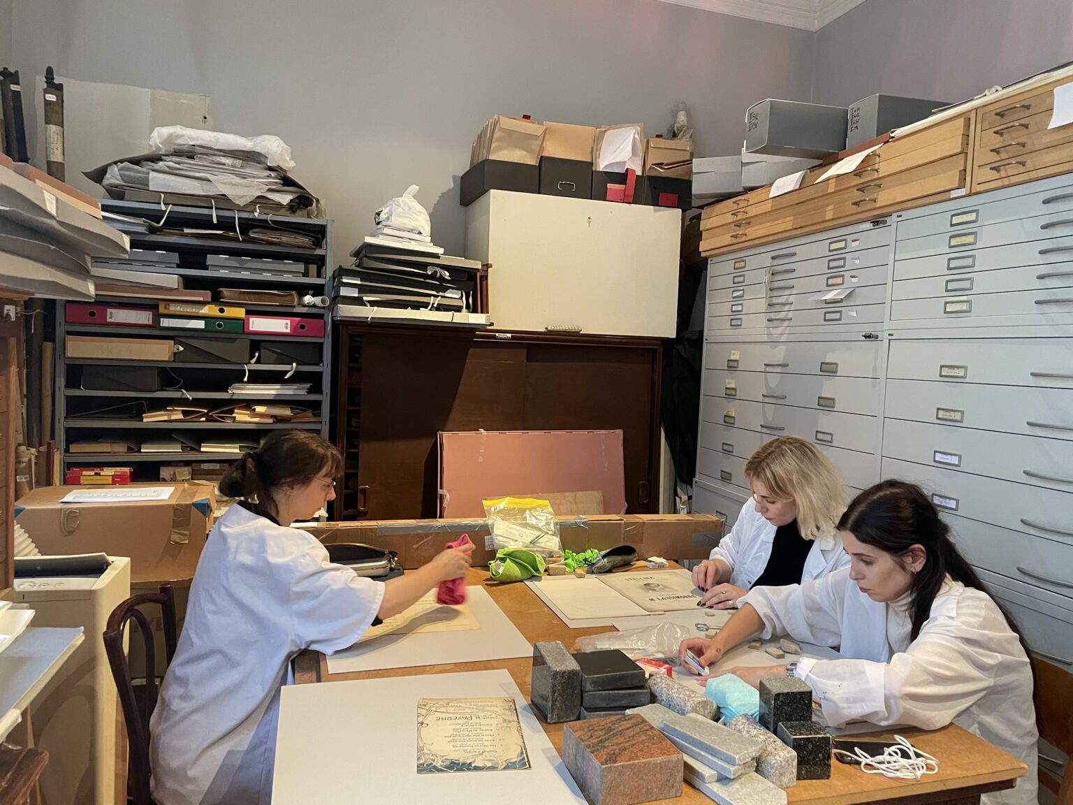 studentki ubrane w białe fartuchy pracują przy zabytkach papierowych.