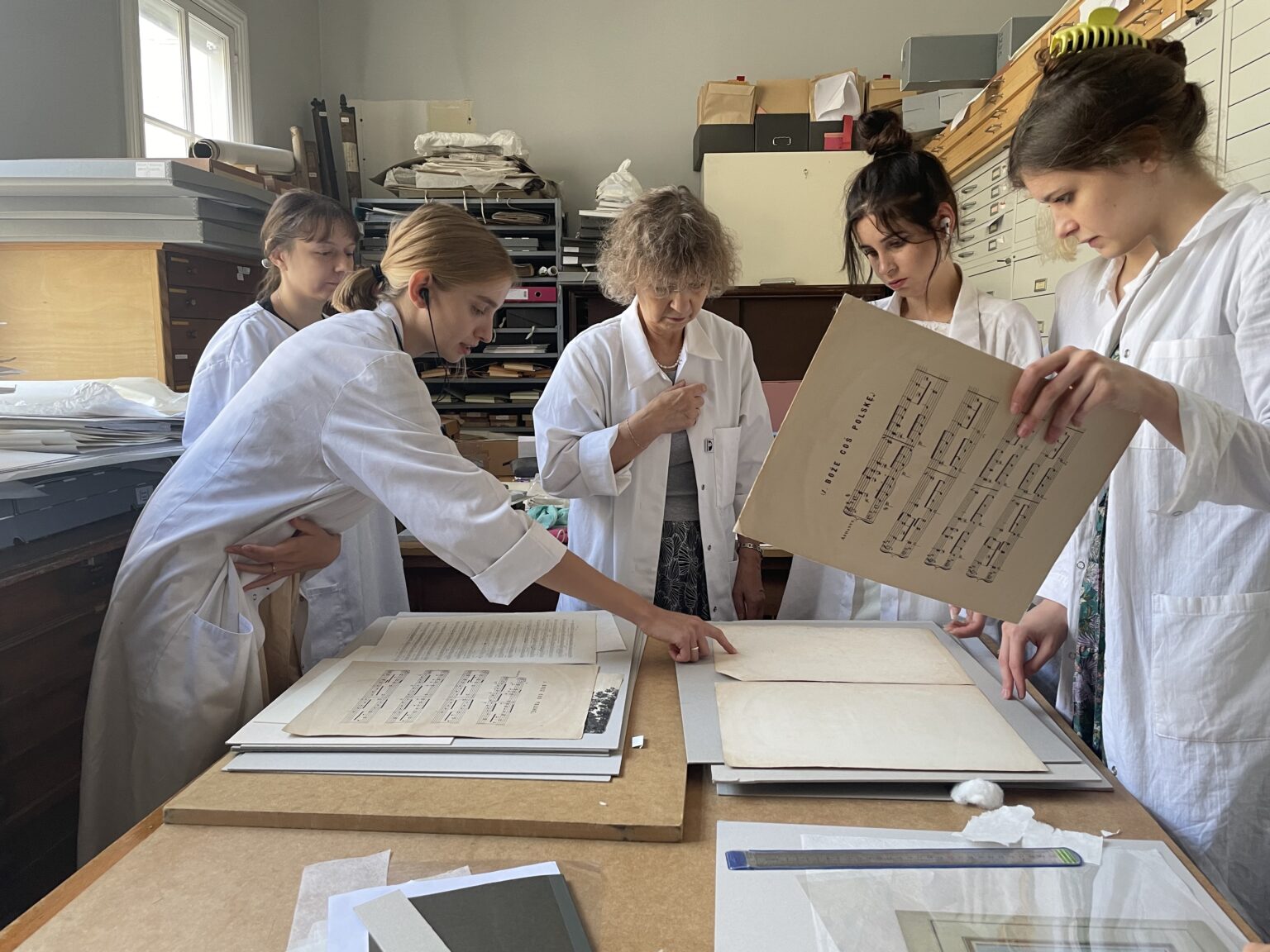 studentki ubrane w białe fartuchy pracują przy zabytkach papierowych.