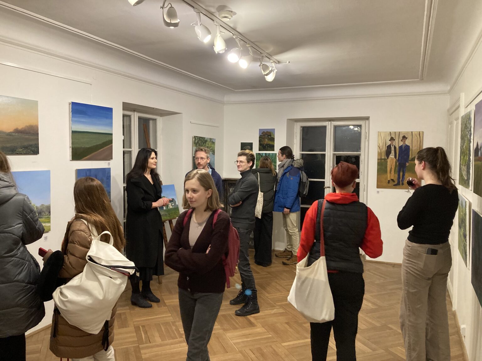 wernisaż wystawy. Grupa ludzi stroi w sali oglądając prace