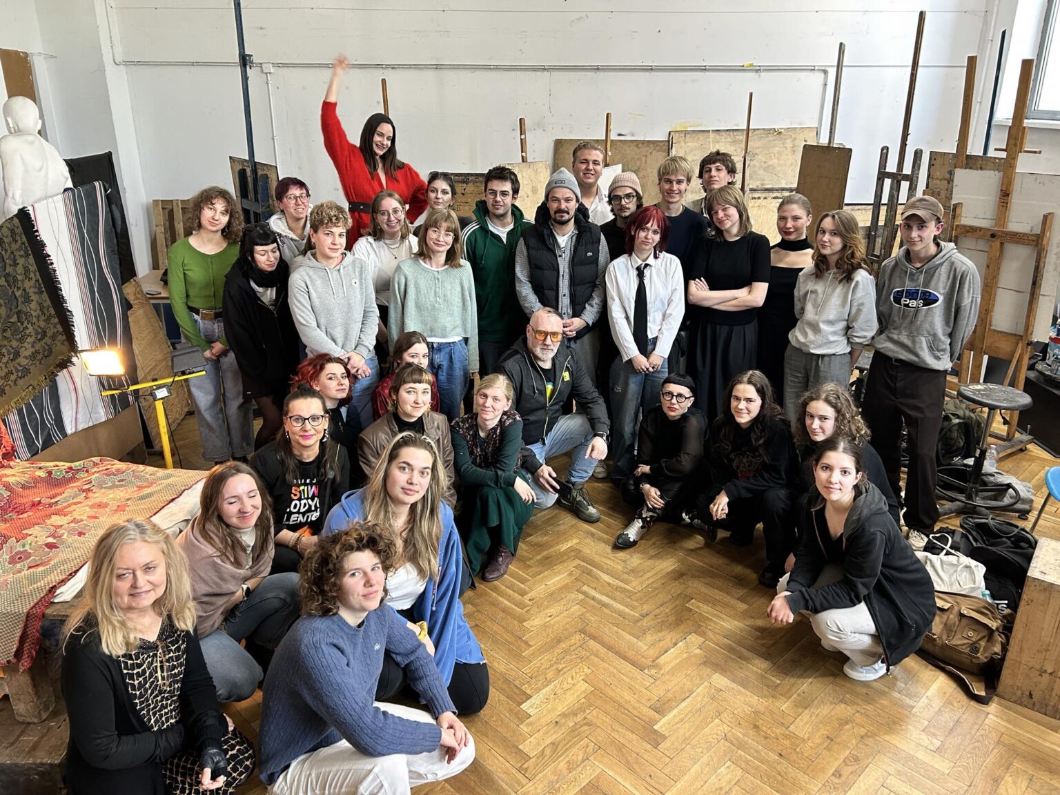 Grupa postaci pozuje na tle sztalug i prac w pracowni