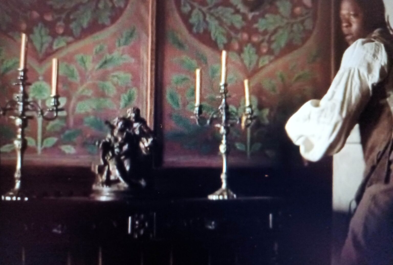 postać po prawej stronie, po lewej dwa świeczniki i rzeźba