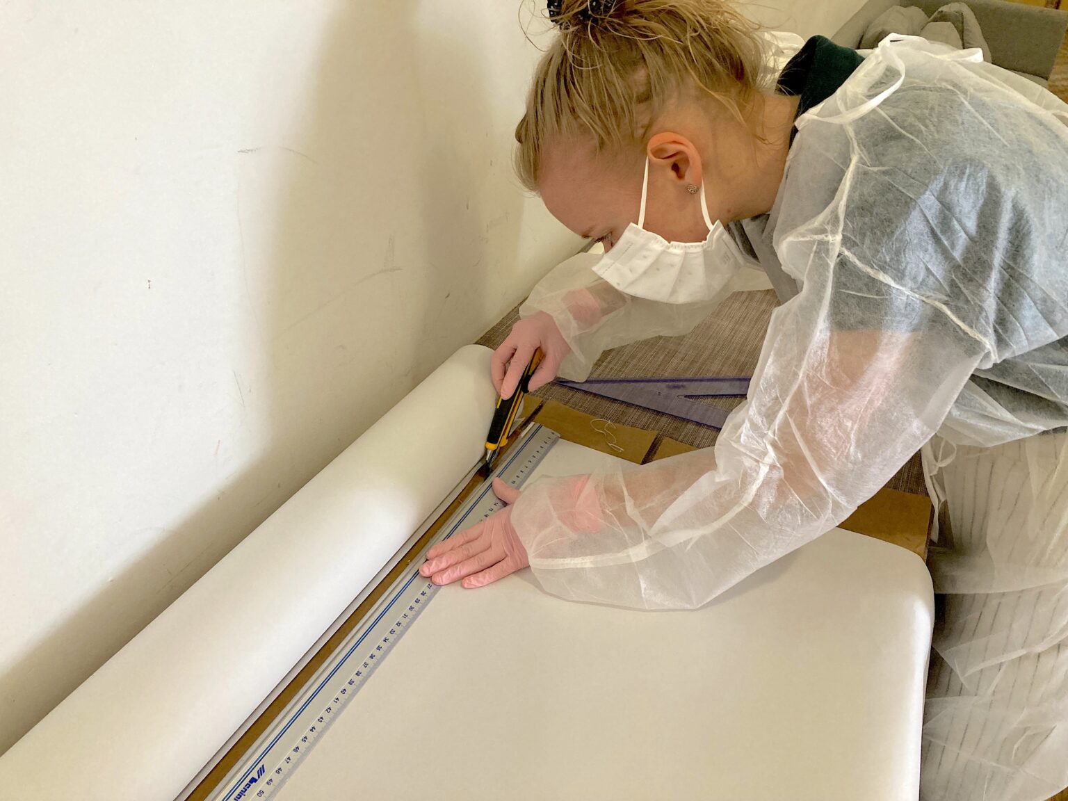 osoba ubrana w biały strój ochrony nachyla się na tkaniną leżącą na stole