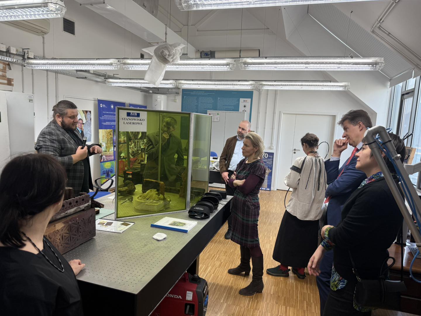 Grupa osób ogląda pokaz czyszczenia laserowego, na stole stoi zielony ekran