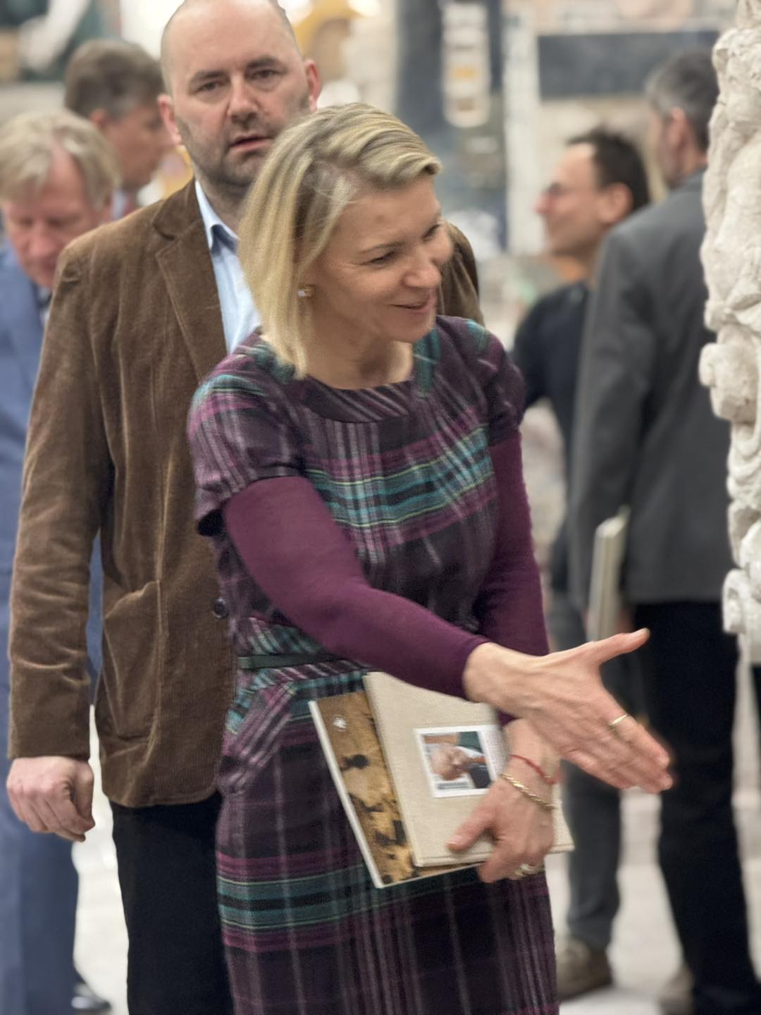 Kobieta z książką w ręku wita się z kimś, w tle inni uczestnicy.