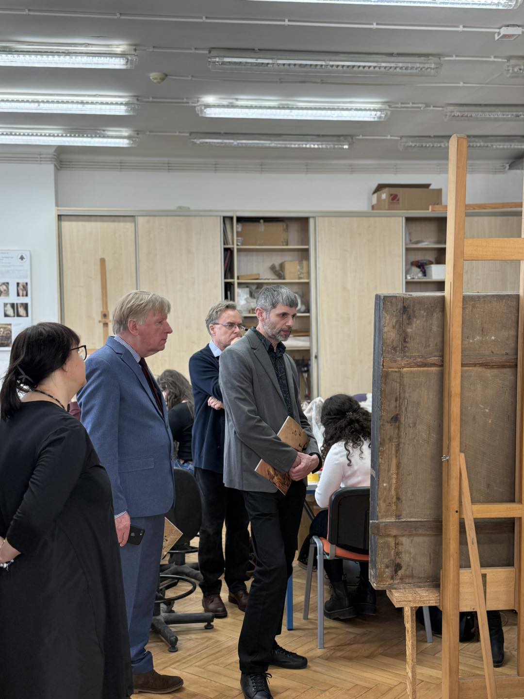 dwóch mężczyzn i kobieta oglądają obraz stojący na sztaludze