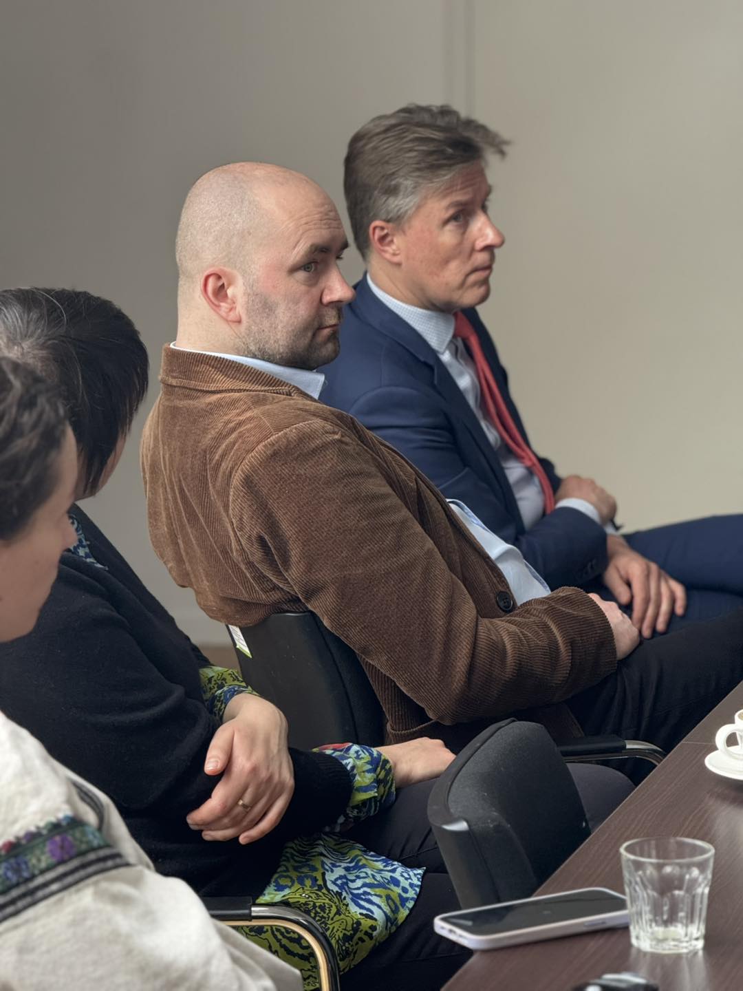 Uczestnicy spotkania siedzący przy stole, słuchający prezentacji.