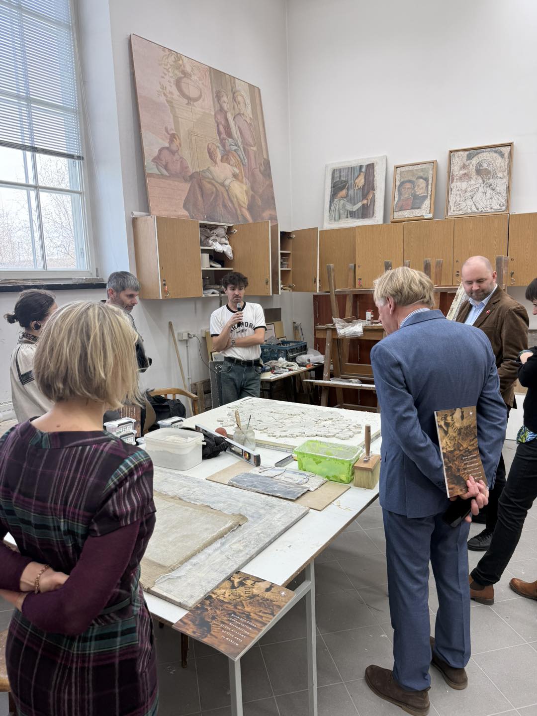 Grupa ludzi stoi wokół stołu, na którym leży fragment malowidła