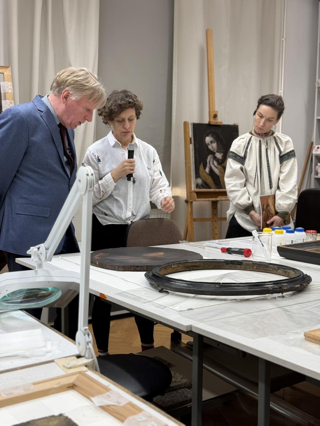 Pokaz prac konserwatorskich przy stole, zbliżenie na ramę obrazu.