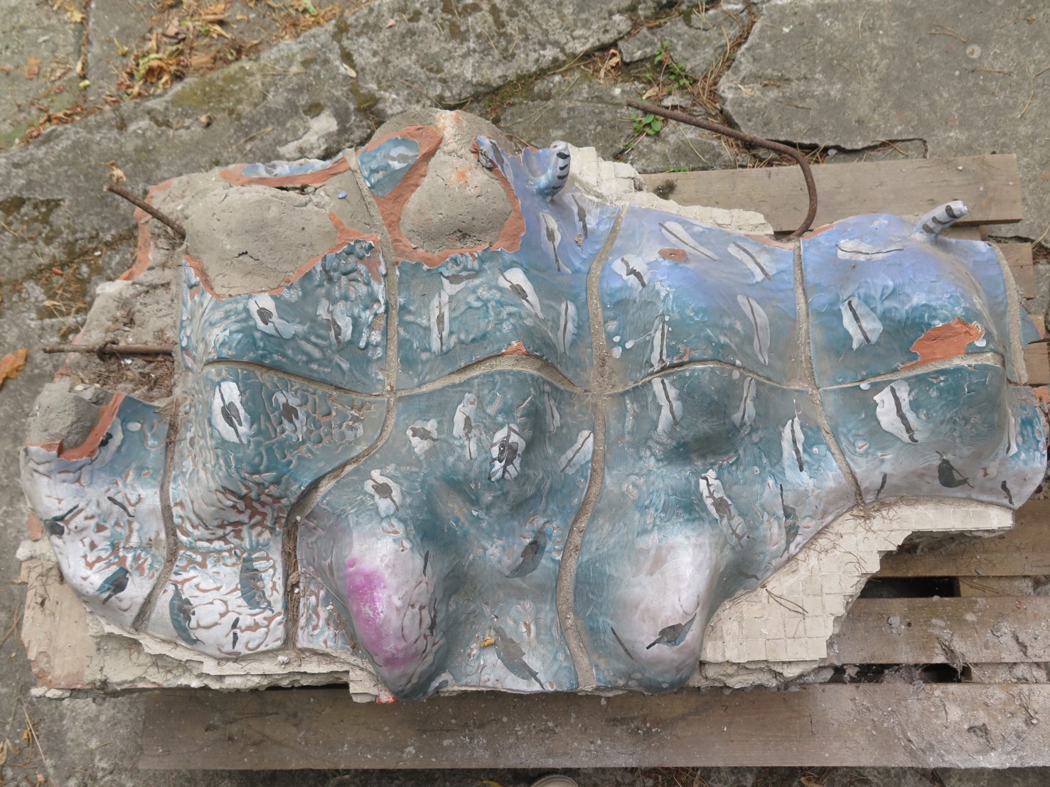 Fragment ceramicznej mozaiki w kształcie ptaka, pokazujący jej stan przed konserwacją – widoczne ubytki i uszkodzenia.