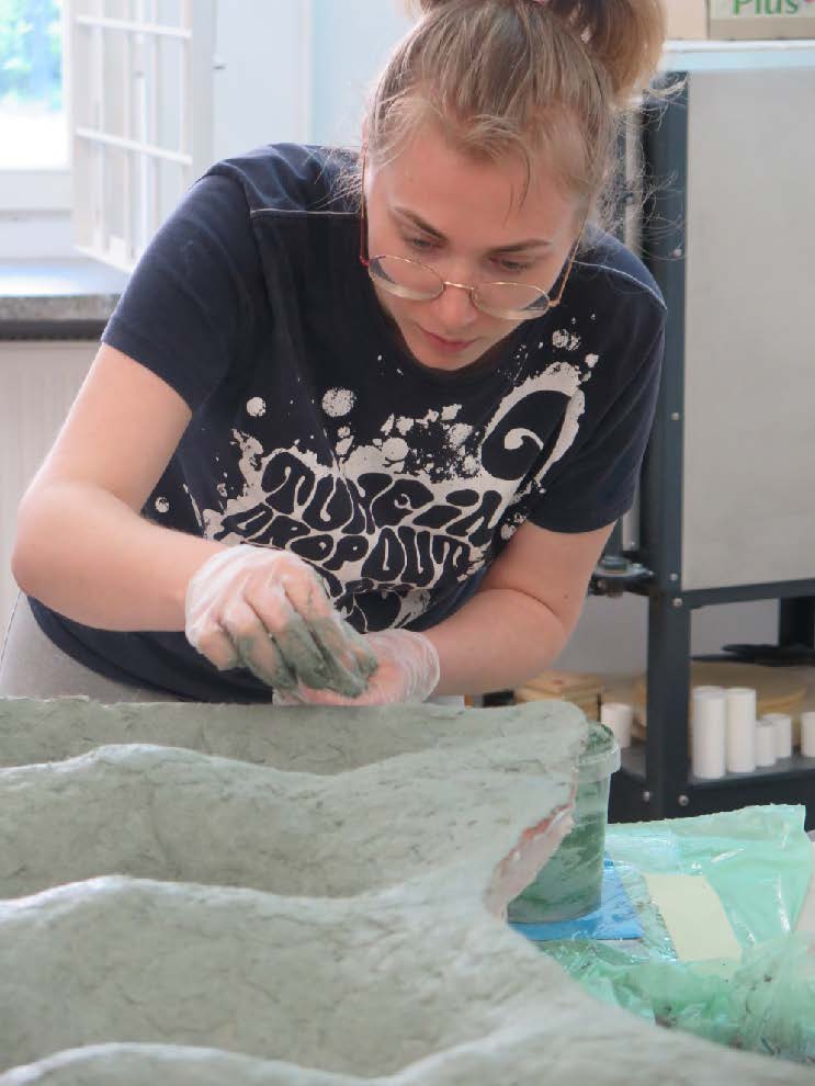 Młoda kobieta pracuje przy konserwacji rzeźbiarskiego fragmentu, nakładając masę na uszkodzoną powierzchnię.