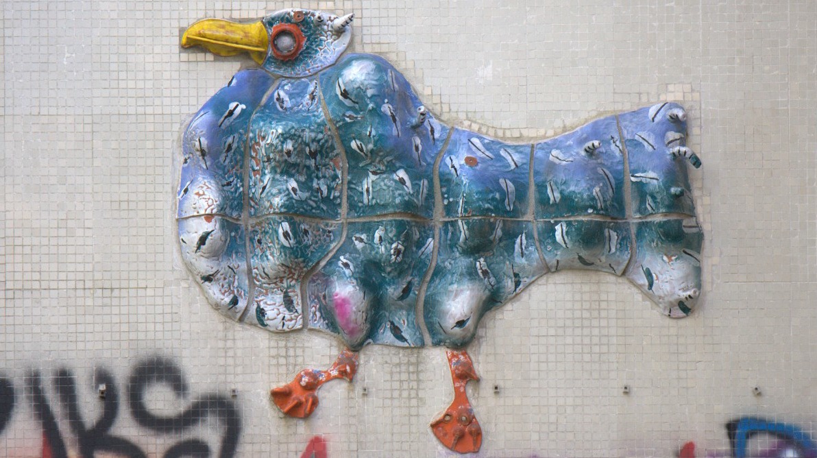 Fragment ceramicznej mozaiki w kształcie ptaka, pokazujący jej stan przed konserwacją – widoczne ubytki i uszkodzenia.