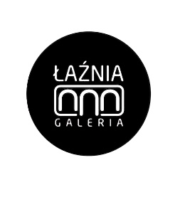 Czarny, okrągły logotyp Łaźni – Galerii z białym napisem „ŁAŹNIA” i stylizowanym znakiem graficznym poniżej, na jasnym tle.